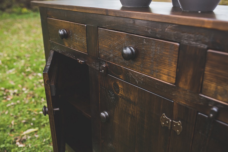Dark brown wooden sideboard showing 2 drawers and 2 cupboards underneath, one which is ajar.