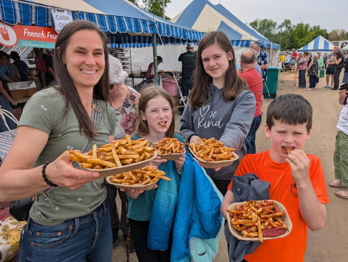 A woman and three children each hold a paper plate of French Fries while others stand in line behind them.