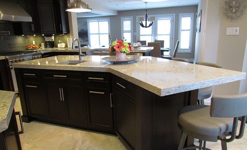 An angled kitchen island with one stool placed at the far end. The kitchen has granite countertops.