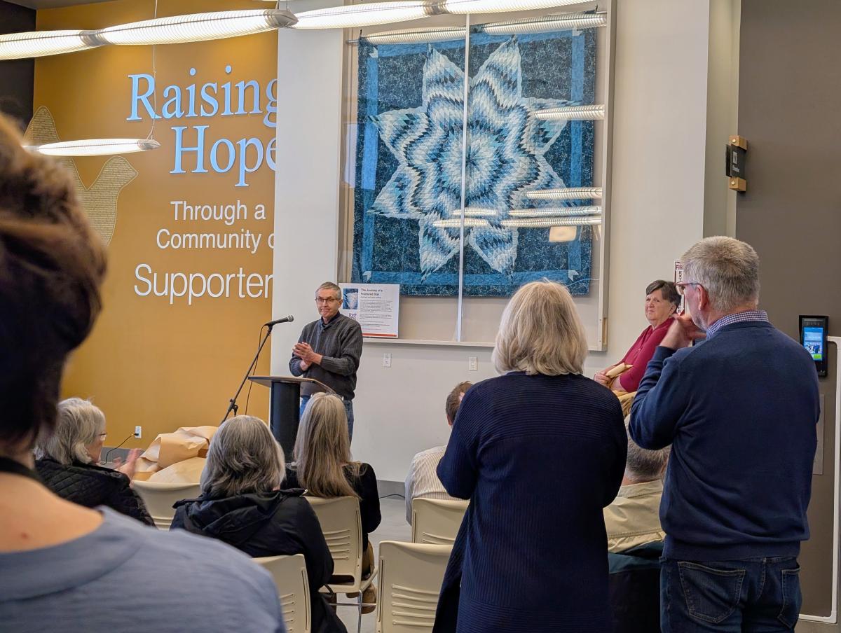 A man speaks to a crowd gathered to see the feature quilt.